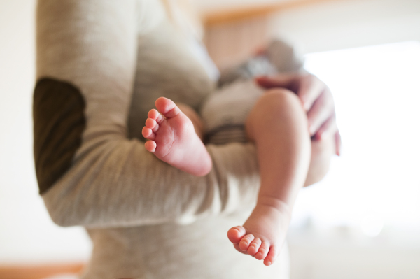 Unrecognizable mother holding her newborn baby son in her arms, close up of legs and hands.