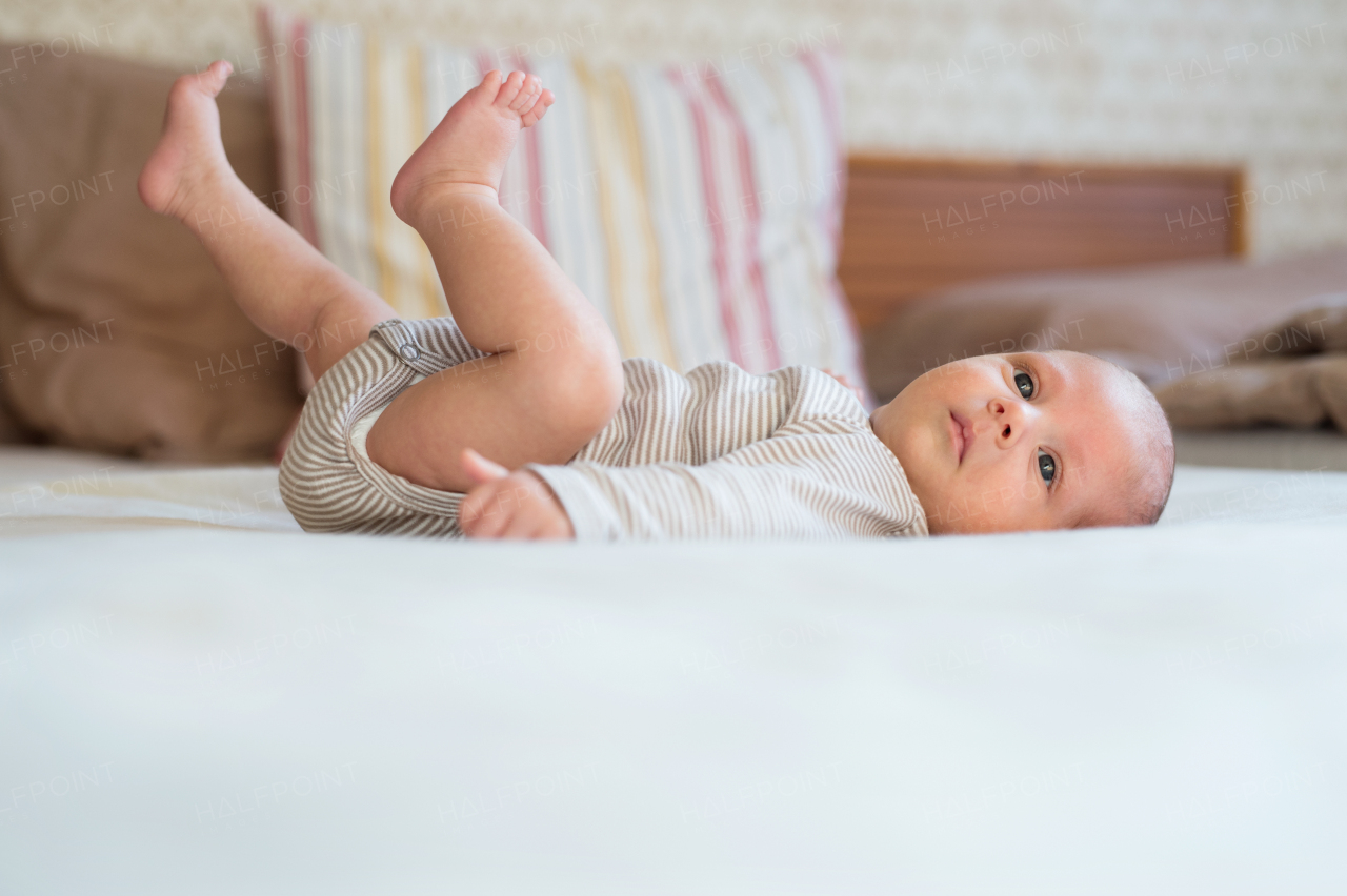 Cute newborn baby boy in brown striped onesie lying on bed, legs in the air