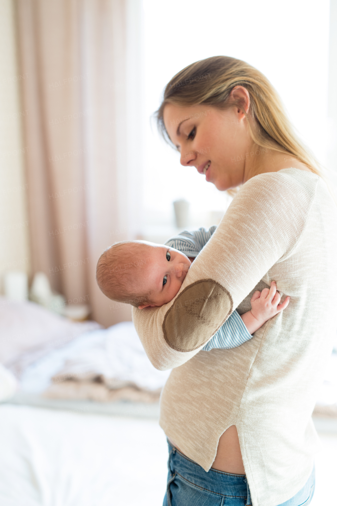 Beautiful young mother holding her baby son in her arms, sitting on bed