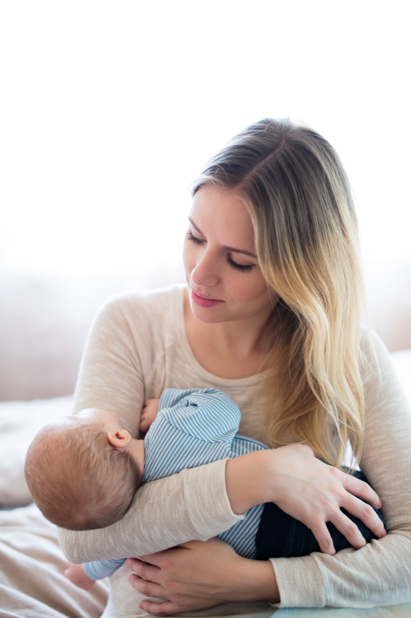 Beautiful young mother holding her baby son in her arms, sitting on bed