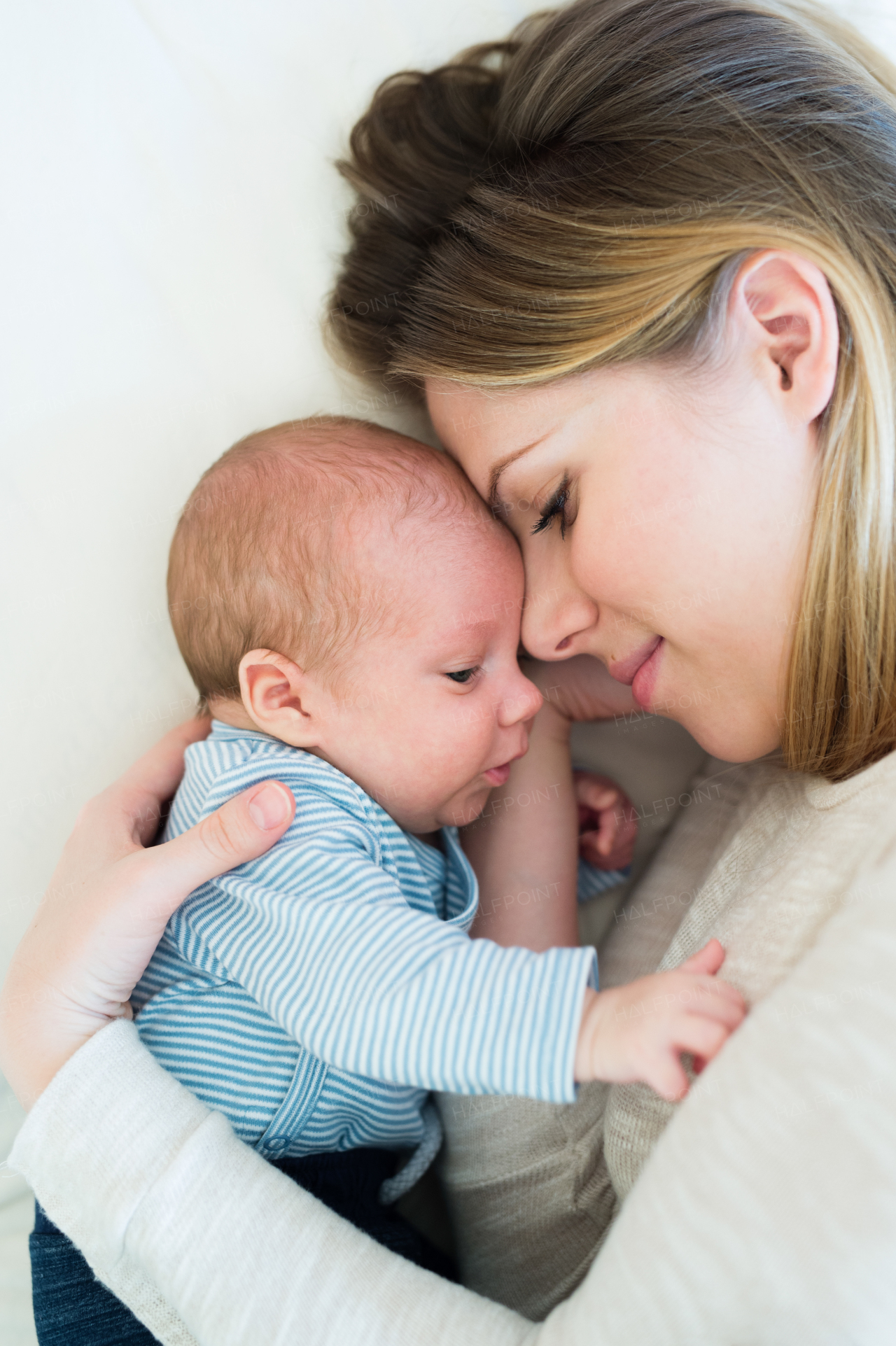 Beautiful young mother with her newborn baby son lying on bed in her bedroom, smiling.