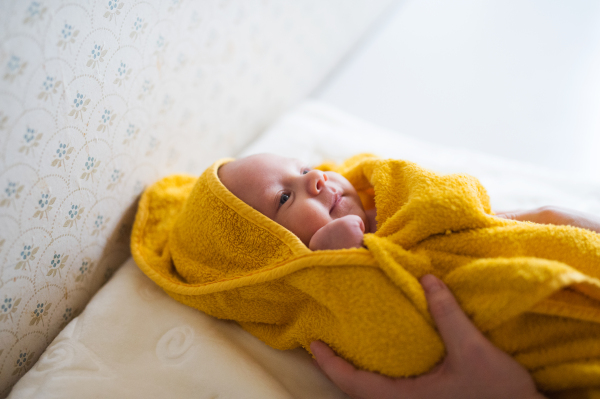 Hands of unrecognizable mother drying her baby son with yellow towel after bathing him. Close up.