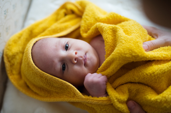 Hands of unrecognizable mother drying her baby son with yellow towel after bathing him. Close up.