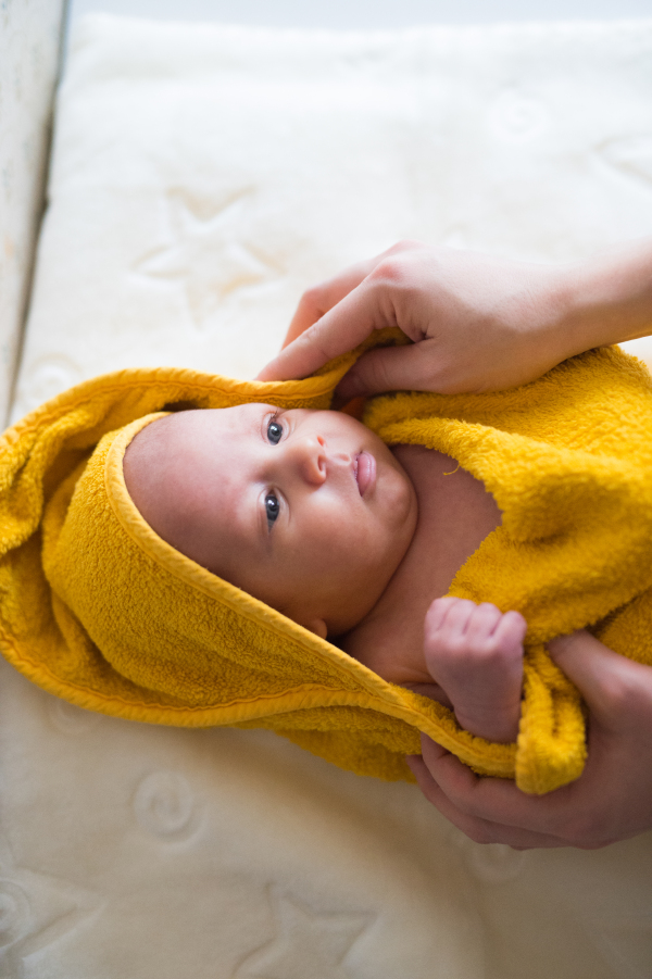 Hands of unrecognizable mother drying her baby son with yellow towel after bathing him. Close up.