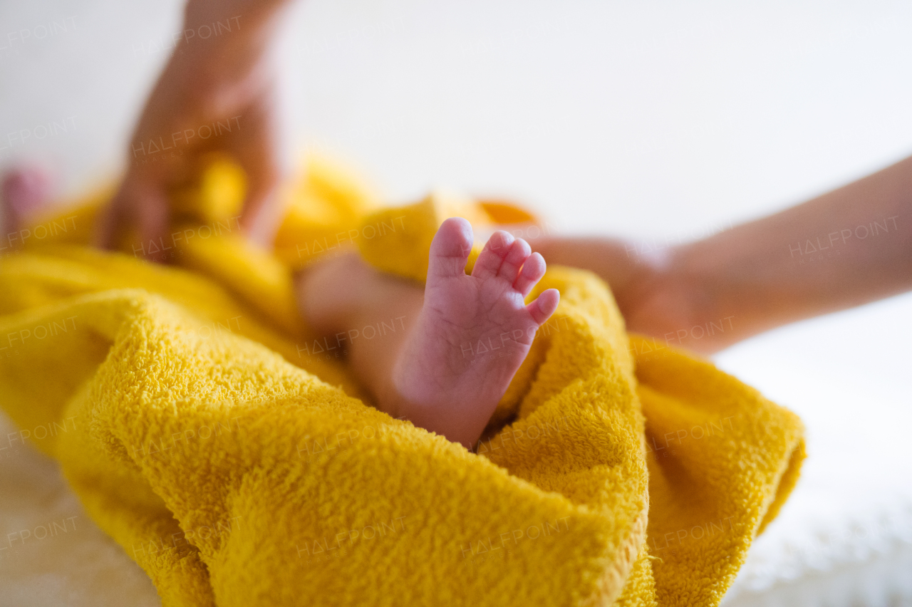 Unrecognizable mother drying her baby son with yellow towel after bathing him. Close up.