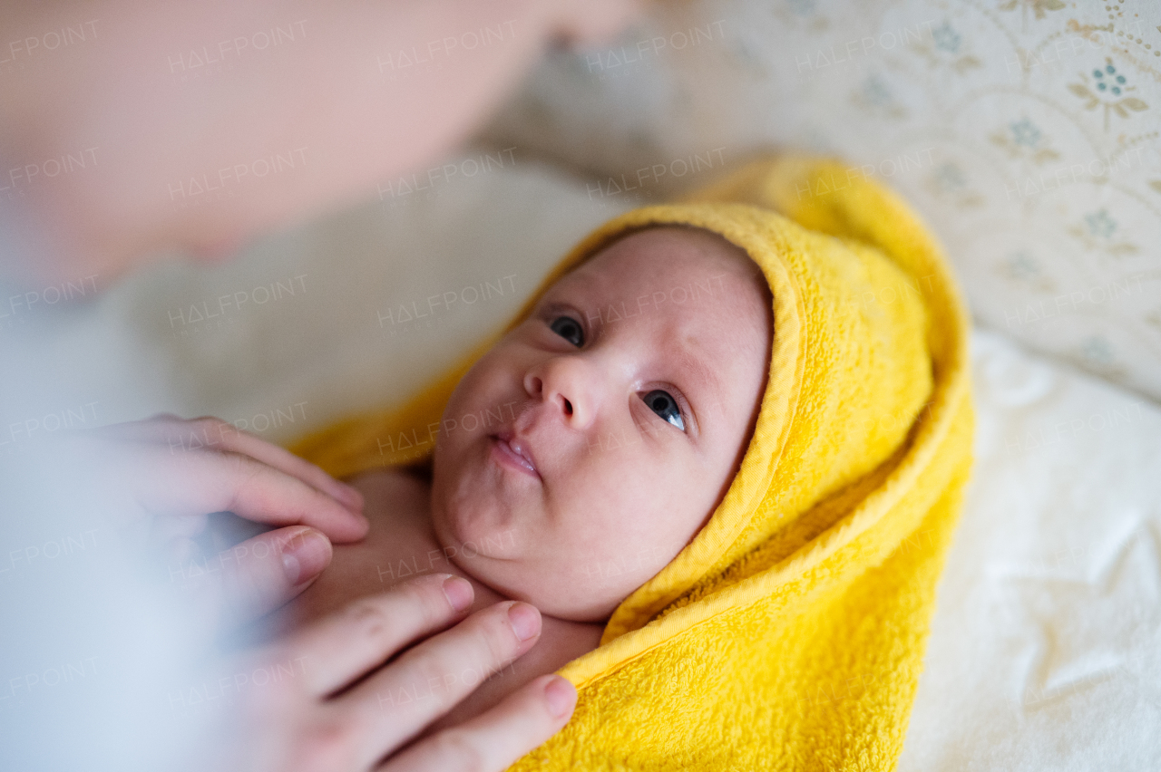 Hands of unrecognizable mother drying her baby son with yellow towel after bathing him. Close up.