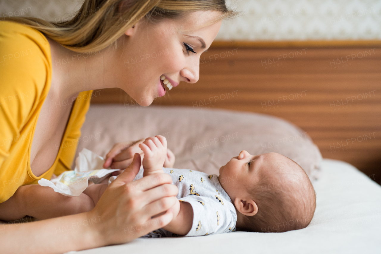 Beautiful young mother with her newborn baby son lying on bed in her bedroom.