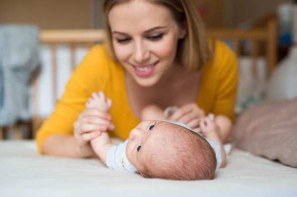 Beautiful young mother with her newborn baby son lying on bed in her bedroom, holding hands.