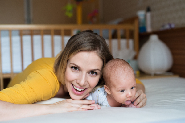 Beautiful young mother with her newborn baby son lying on bed in her bedroom, hugging him. Boy sticking tongue out.