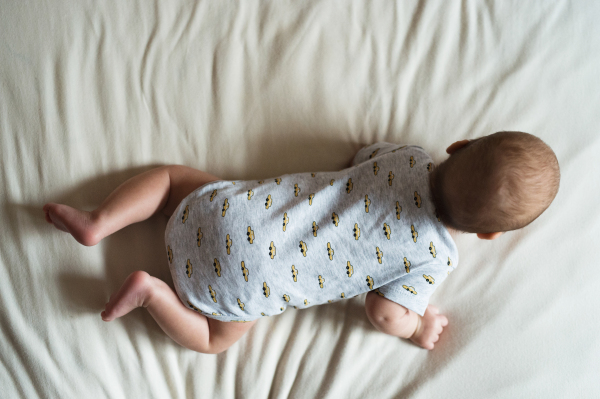 Cute newborn baby boy lying on bed, close up. Rear view.