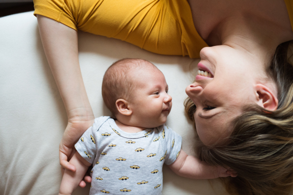 Beautiful young mother with her newborn baby son lying on bed in her bedroom, smiling.