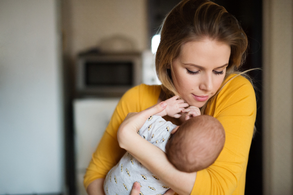 Beautiful young mother in yellow t-shirt holding her baby son in her arms