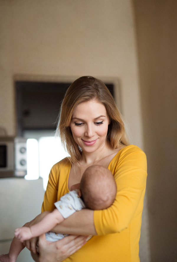 Beautiful young mother in yellow t-shirt holding her baby son in her arms