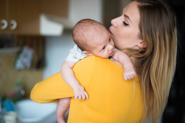 Beautiful young mother in yellow t-shirt holding her baby son in her arms