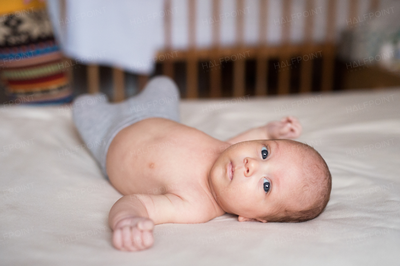 Cute newborn baby boy with blue eyes lying on bed, close up