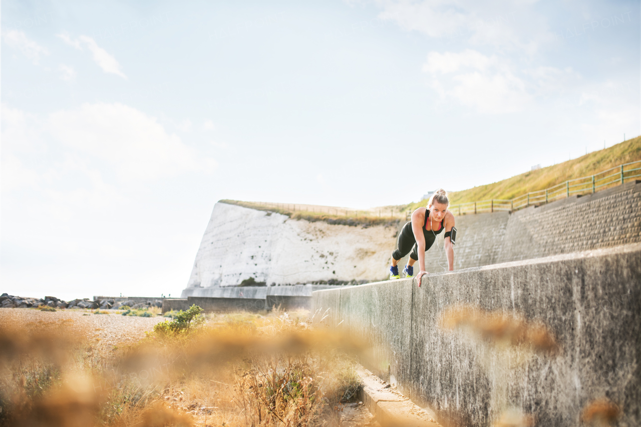 Young woman doing fitness plank position exercises outside by the seaside. Copy space.