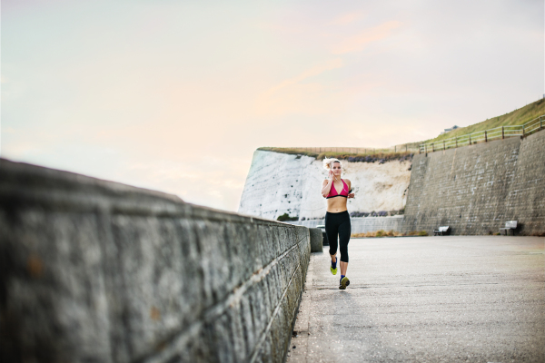 Young sporty woman runner with earphones running outside in nature, listening to music.