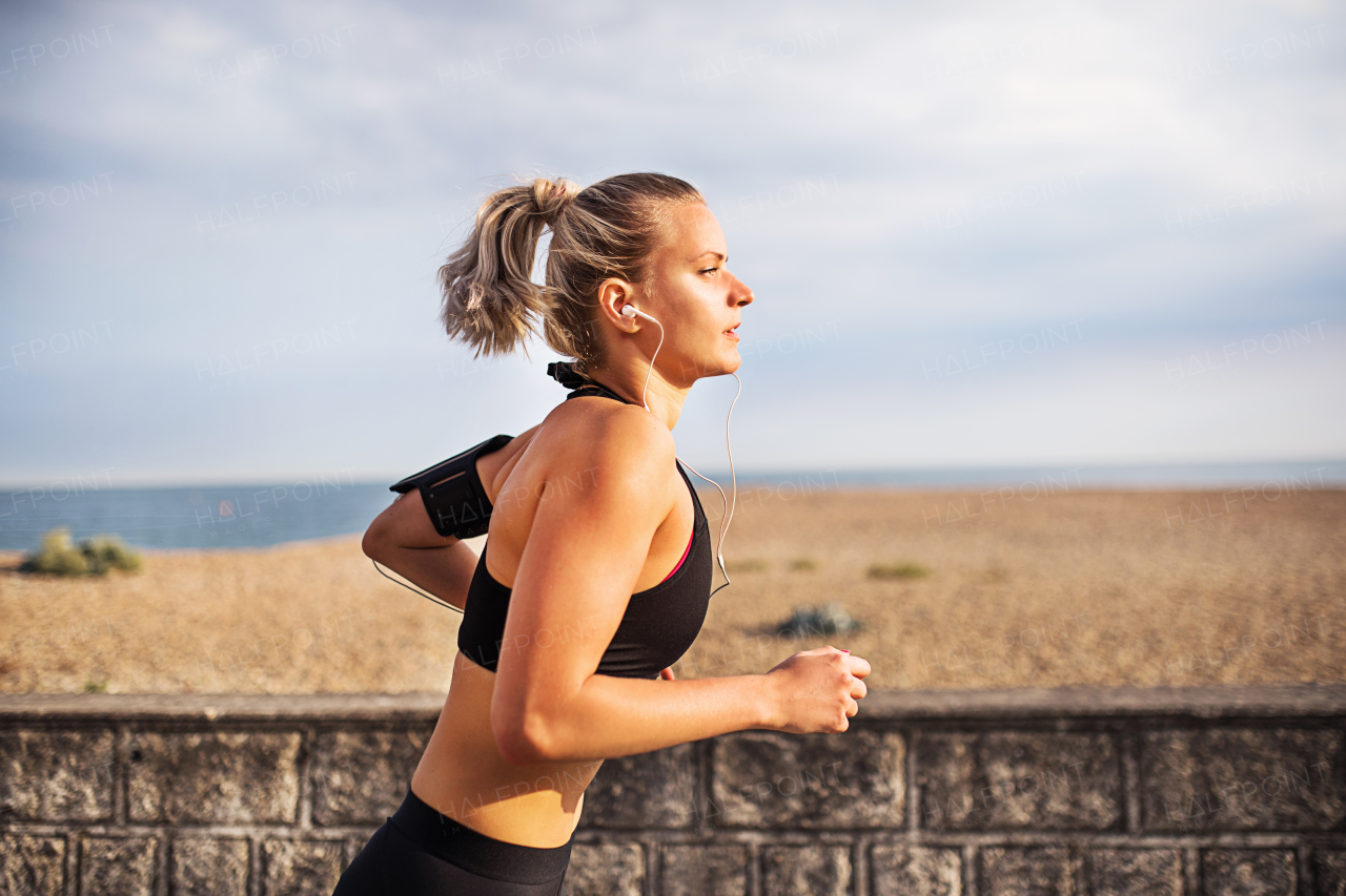 Young sporty woman runner with earphones running outside on the beach in nature, listening to music.