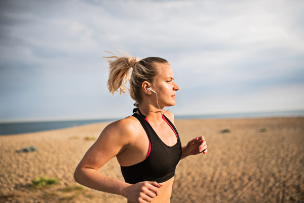 Young sporty woman runner with earphones running outside on the beach in nature, listening to music.