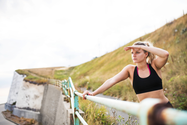 Young sporty woman runner in black activewear standing outside in nature, resting. Copy space.