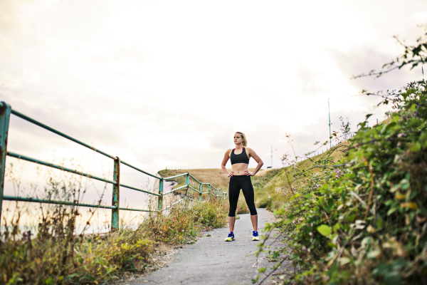 Young sporty woman runner in black activewear standing outside in nature, resting. Copy space.