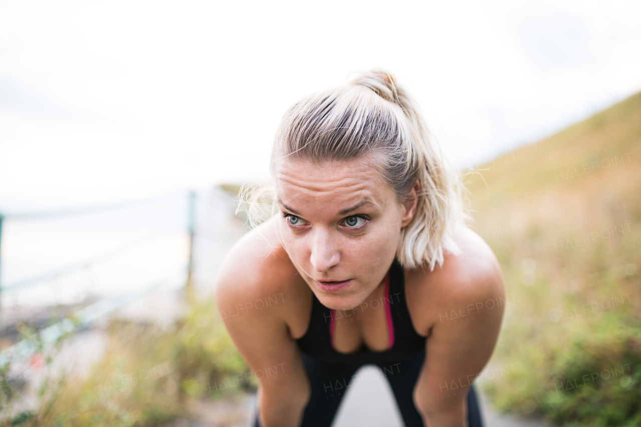 Close-up of young sporty woman runner outside by the sea, resting.