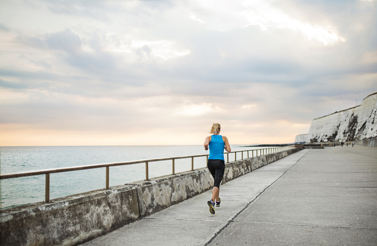 Rear view of young sporty woman runner running on the beach outside. Copy space.