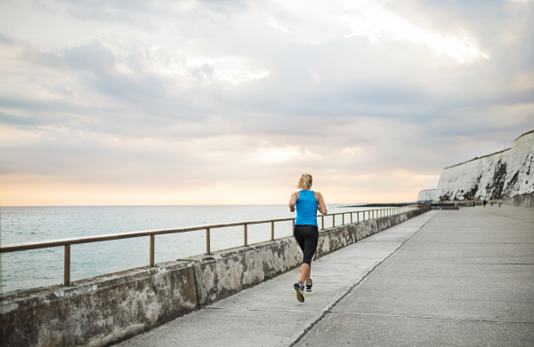 Rear view of young sporty woman runner running on the beach outside. Copy space.