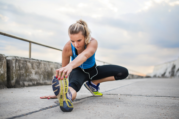 Young sporty woman runner with earphones stretching outside on a footpath in nature. Copy space.