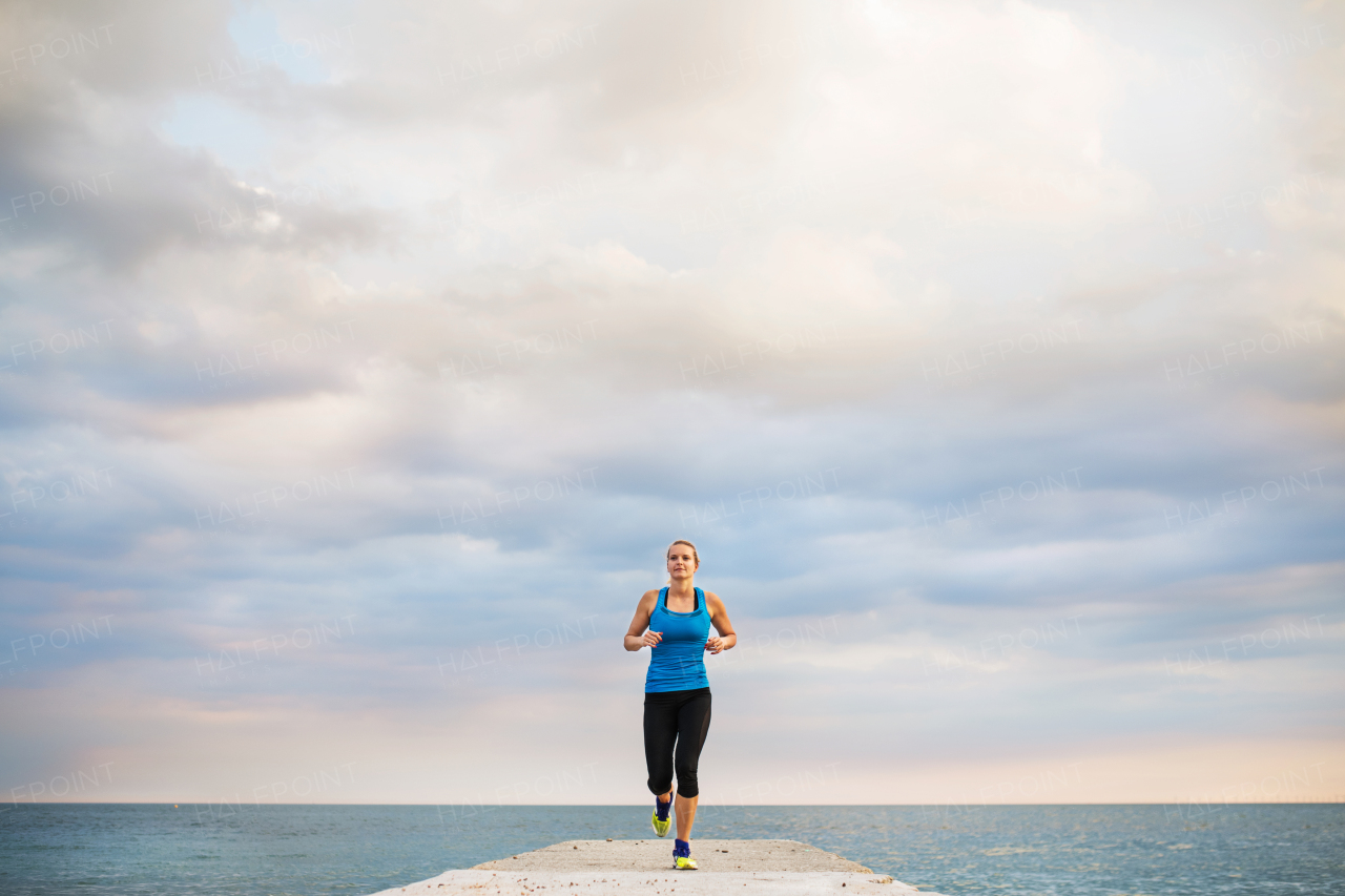 A young sporty woman running outside on a pier, by the ocean. Copy space.