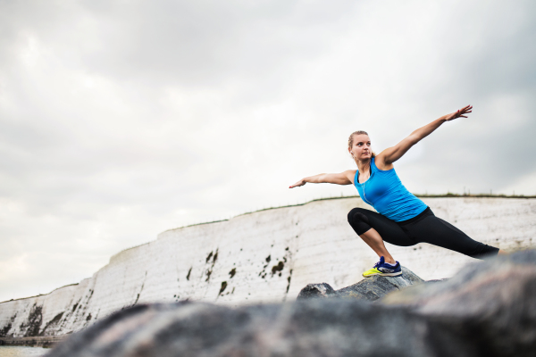 Young sporty woman runner with earphones stretching outside on the beach in nature. Copy space.