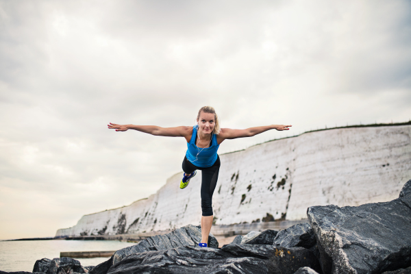 Young sporty woman runner with earphones stretching outside on the beach in nature. Copy space.