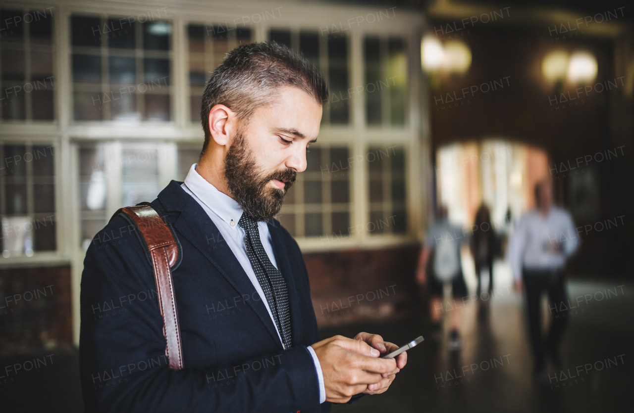 A hipster businessman with smartphone standing indoors in the city, texting. Copy space.