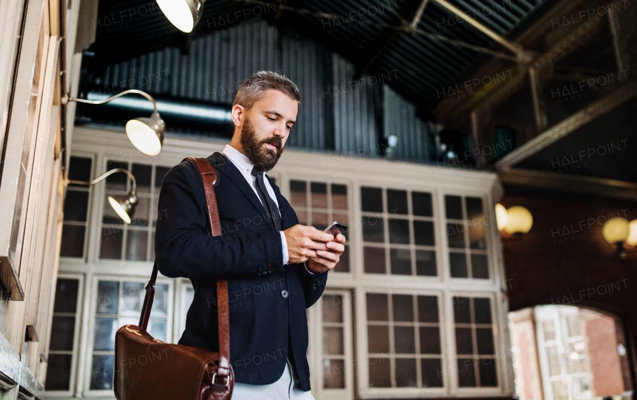 A waist up portrait of businessman with smartphone standing in city, text messaging.