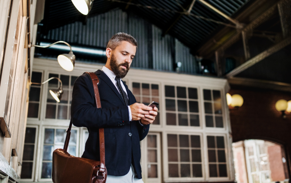 A waist up portrait of businessman with smartphone standing in city, text messaging.