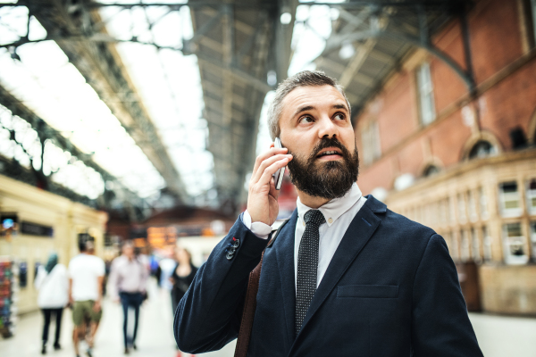 Happy businessman with smartphone on the trian station in London, making a phone call.