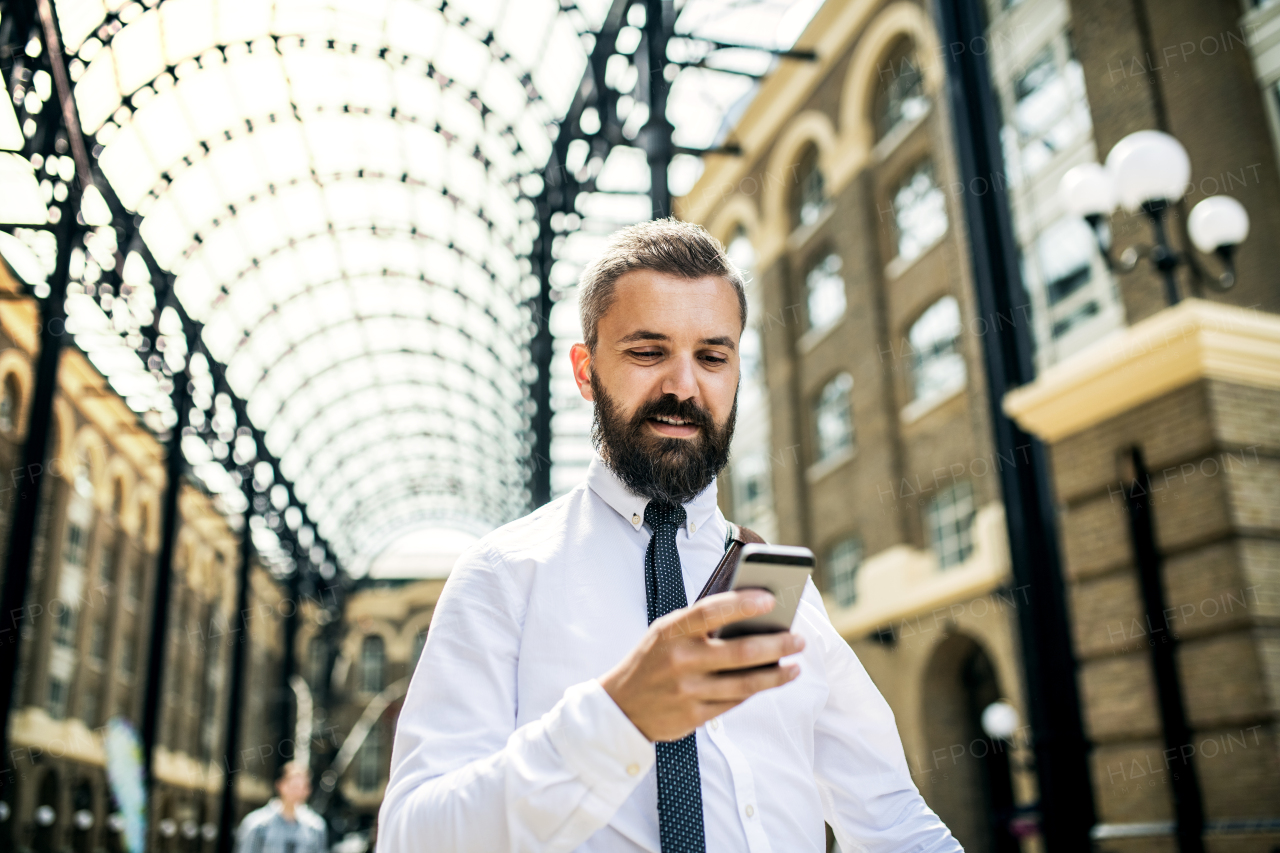 Happy businessman with smartphone on the trian station in London, text messaging.