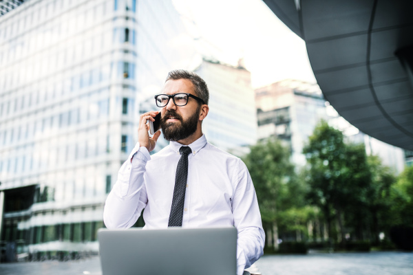 Hipster businessman with laptop and smartphone in the city, making a phone call.