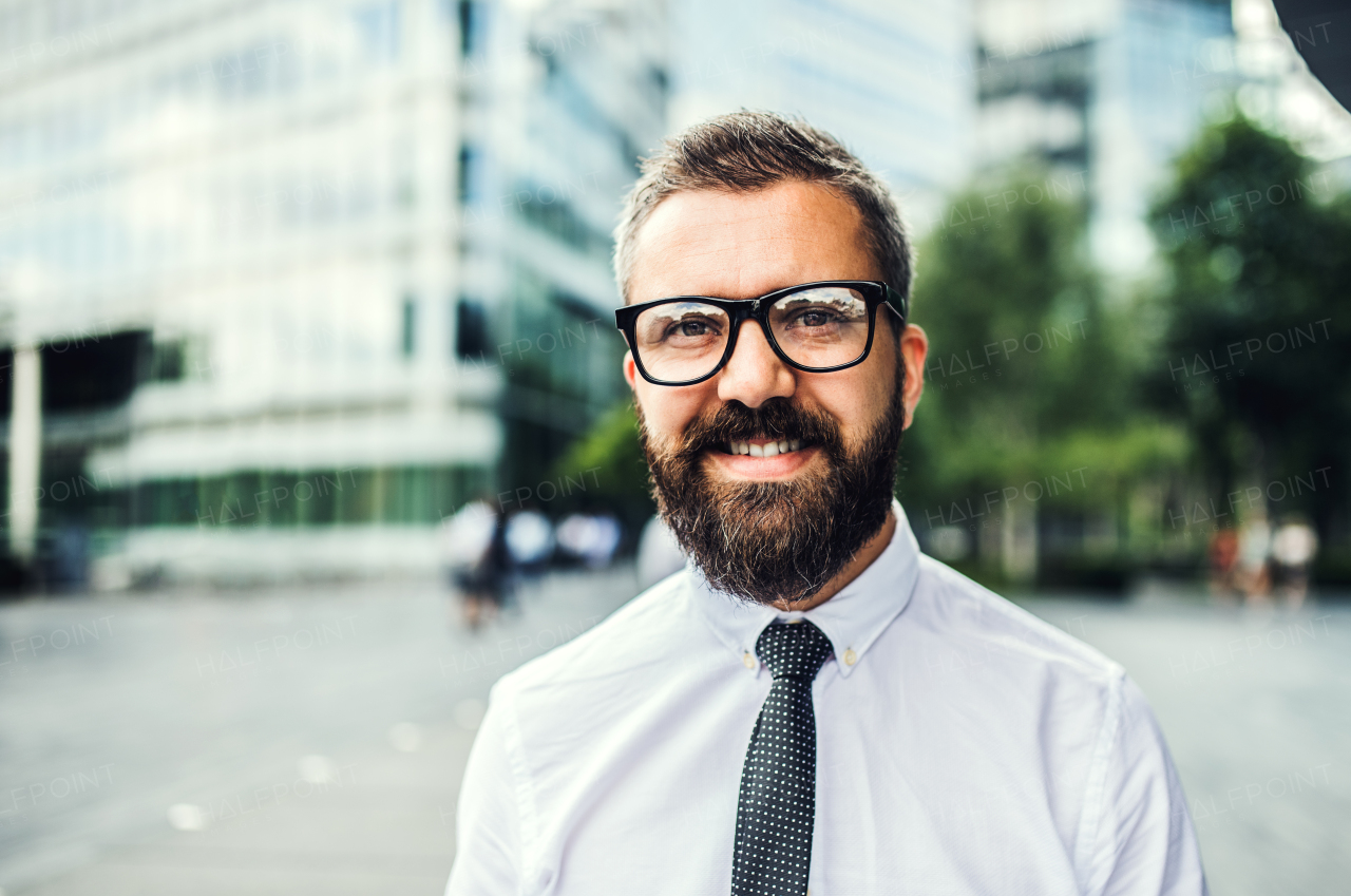 A close-up portrait of hipster businessman with glasses standing in the city. Copy space.