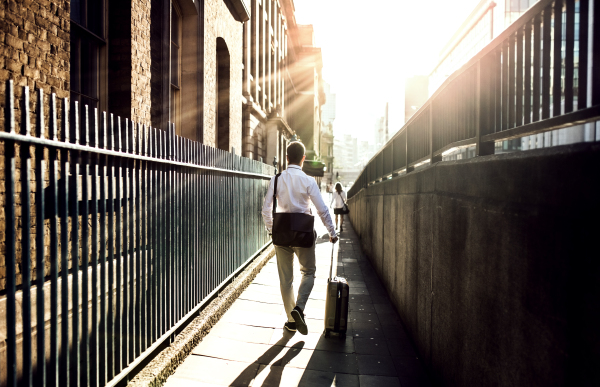 Rear view of businessman with laptop bag and suitcase walking up the street in London. Copy space.