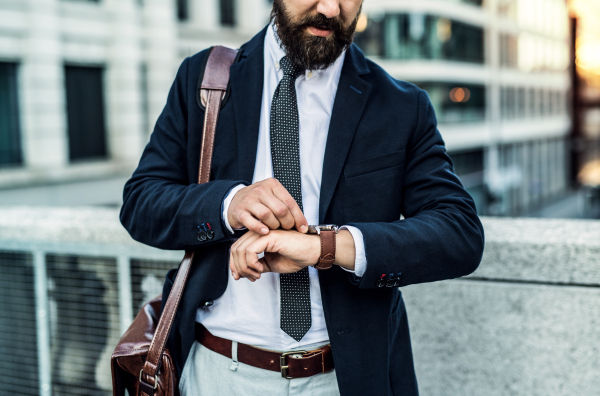 Unrecognizable businessman with laptop suitcase standing on the street in city, checking the time.