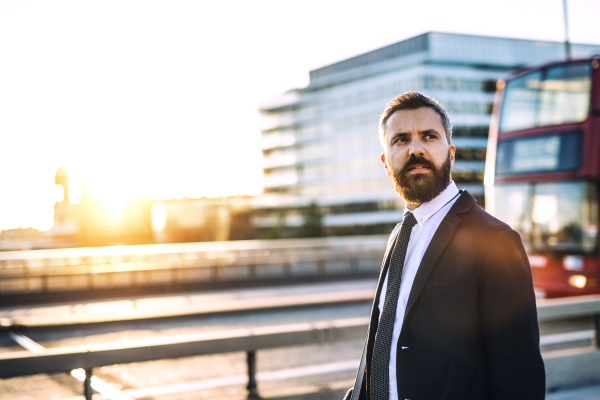 Hipster businessman with jacket and tie walking along the road in London at sunset. Copy space.