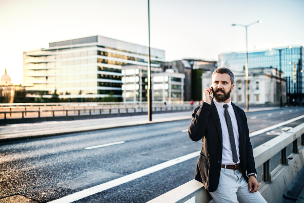 Serious hipster with businessman with smartphone standing outdoors in the city, making a phone call.