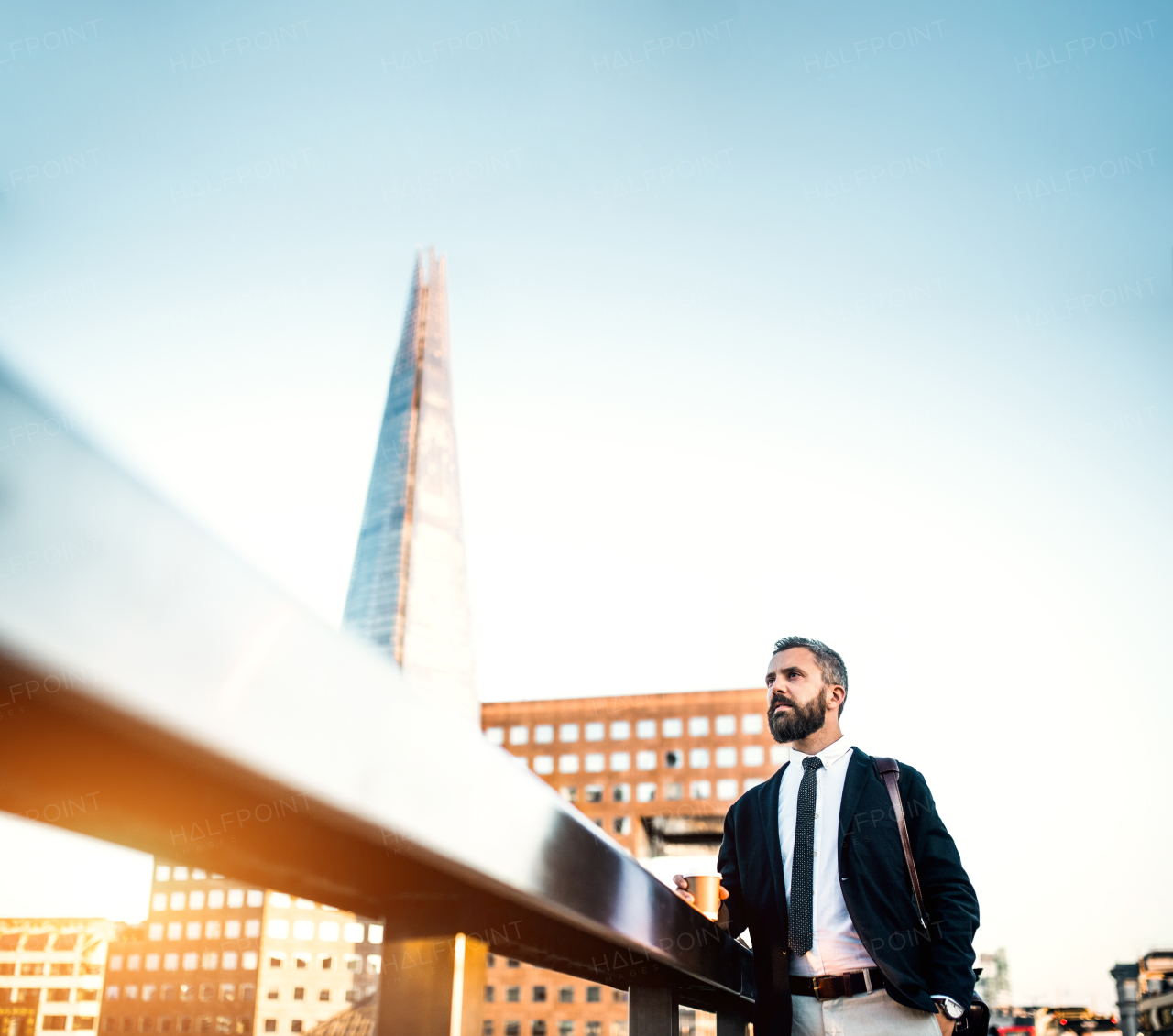 Mature hipster businessman with coffee in a paper cup standing on the bridge in London. Copy space.