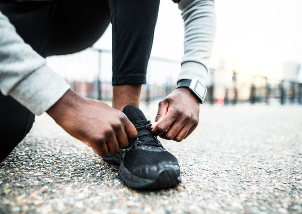 A close-up of an unrecognizable young sporty black man runner tying shoelaces before running outside in a city.