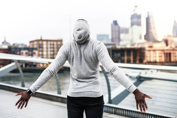 Rear view of a black man runner resting on the bridge in a city, arms stretched.