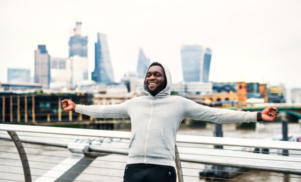 Happy black man runner leaning on railing on the bridge in a city, resting.