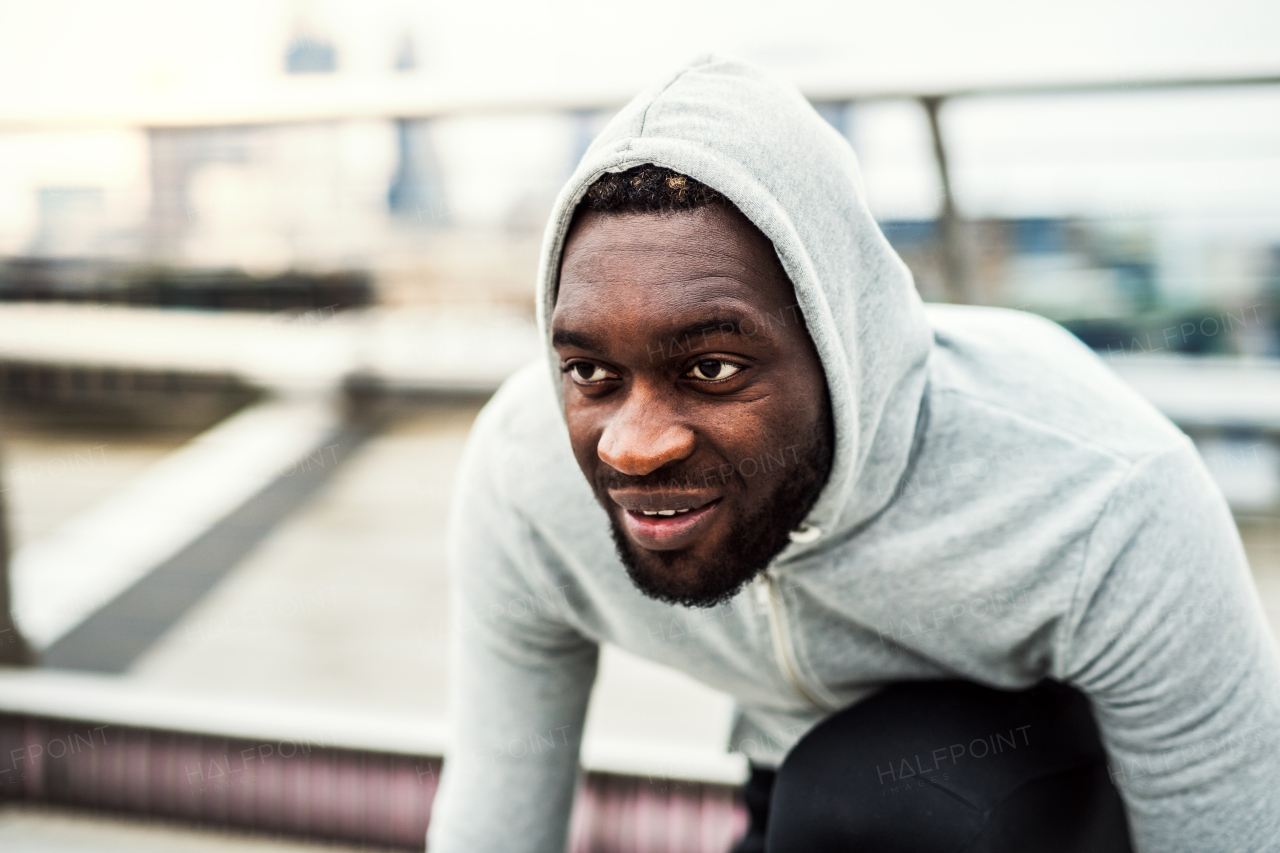 Young sporty black man runner with smartwatch in starting position before running on the bridge outside in a city. A close-up.