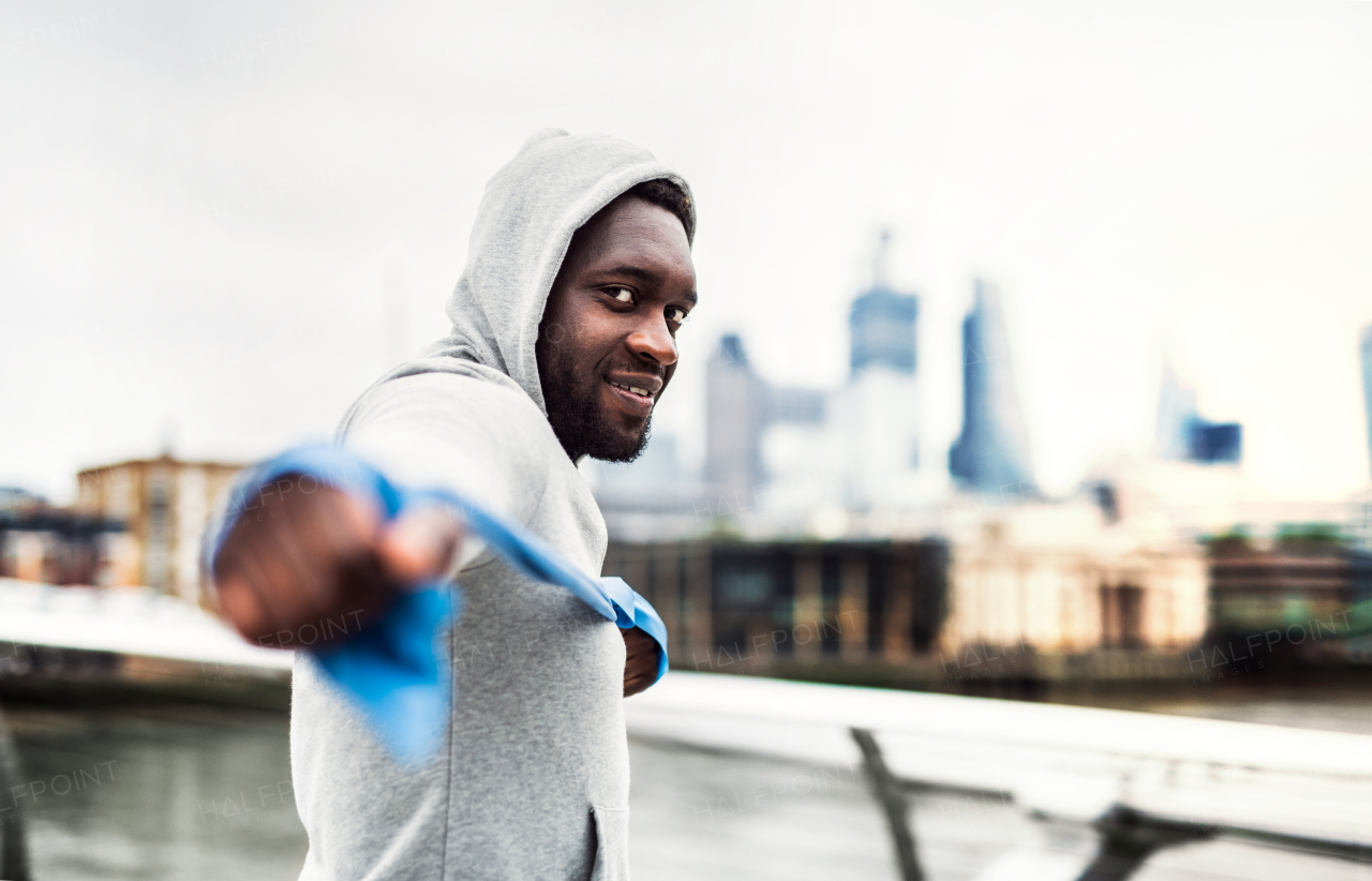 Young active black sportsman exercising with elastic rubber bands on the bridge in London.