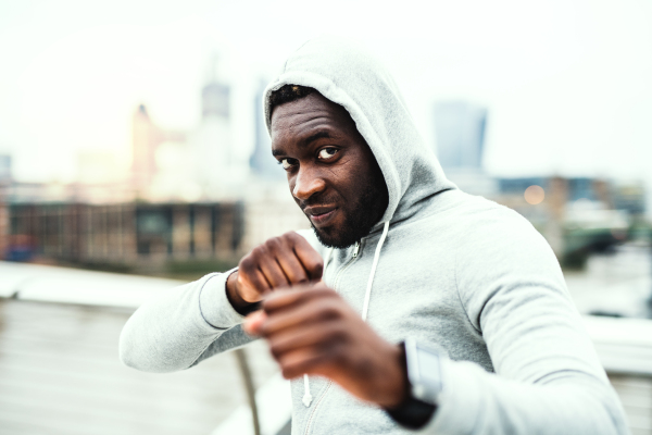 A close-up of a young active black sportsman standing in boxing position in a city.